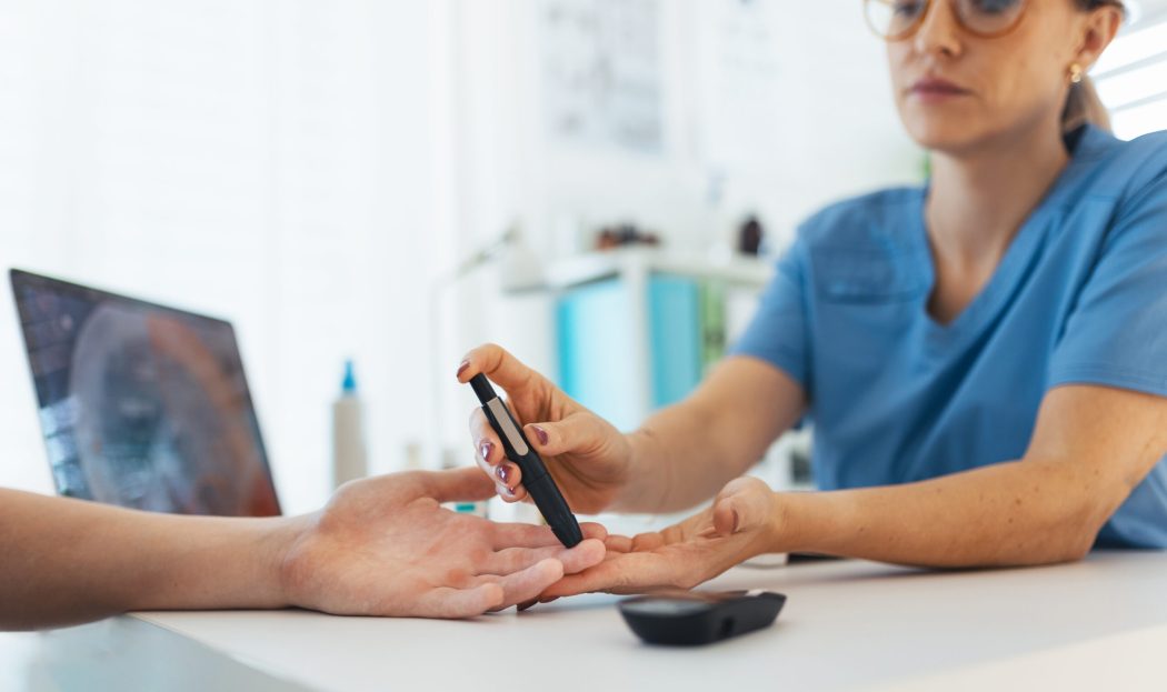 Diabetologist doctor testing blood sample on blood sugar meter in diabetes clinic. Doctor taking blood sample from boy's finger. Paediatric diabetes in teenage boy, young man.